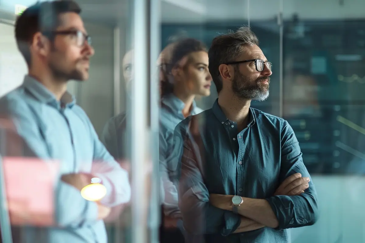 Three colleagues with crossed arms looking skeptically through a glass wall